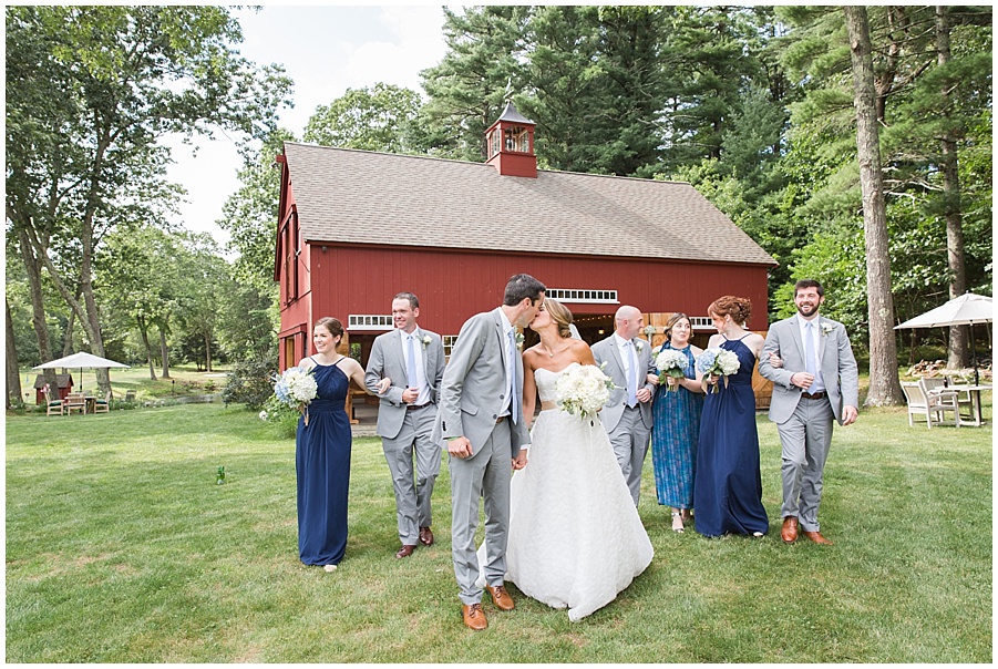 bride and groom kiss in front of bridal party and red barn