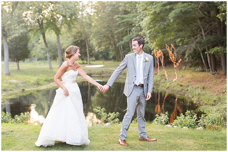 bride and groom walk by pond with twinkle lights 
