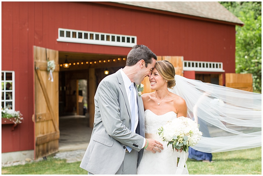 bride and groom nuzzle in front of red barn 