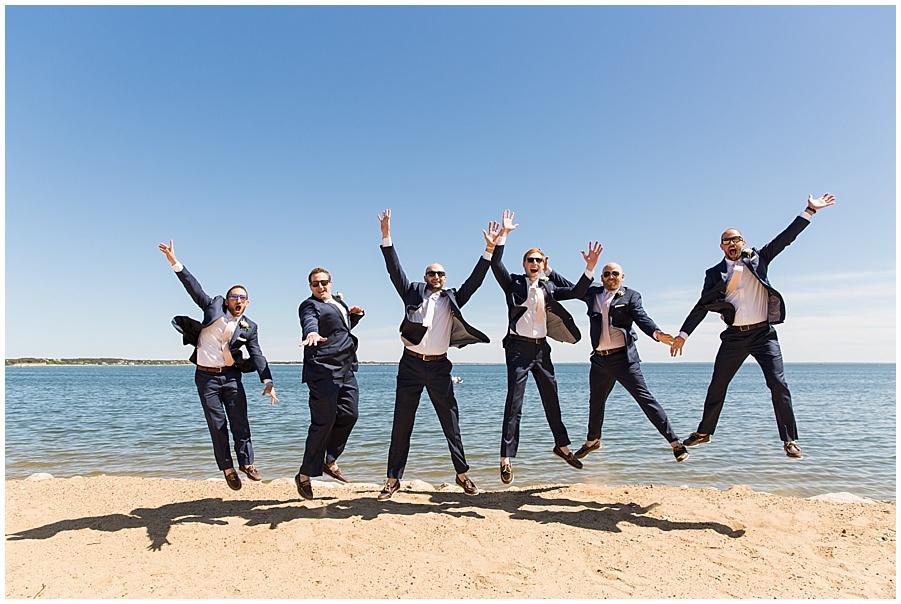 groom and groomsmen jump in the air on the beach 