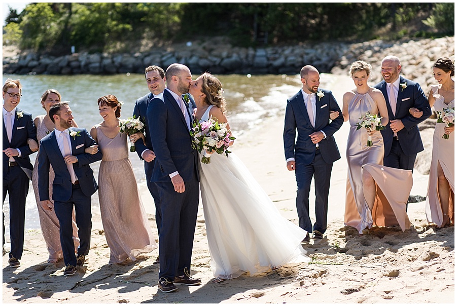 bride and groom walk down beach with bridal party 